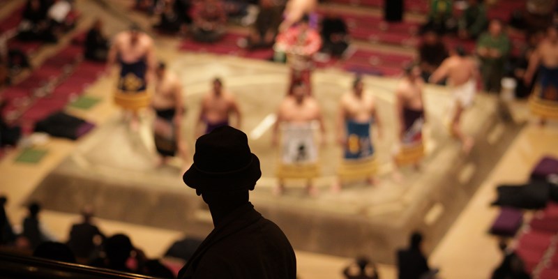 Silhouette of an elderly man watching sumo wrestlers standing in a ceremonial ring
